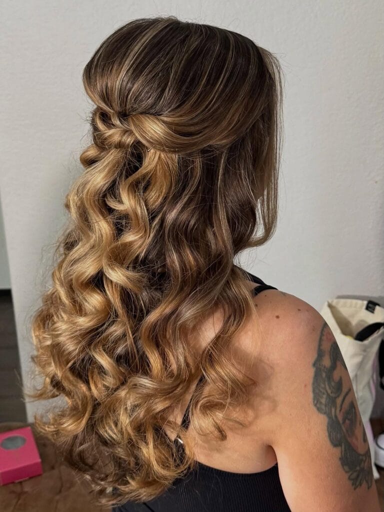 Long wavy hair styled half up with soft curls and warm highlighted tones.
