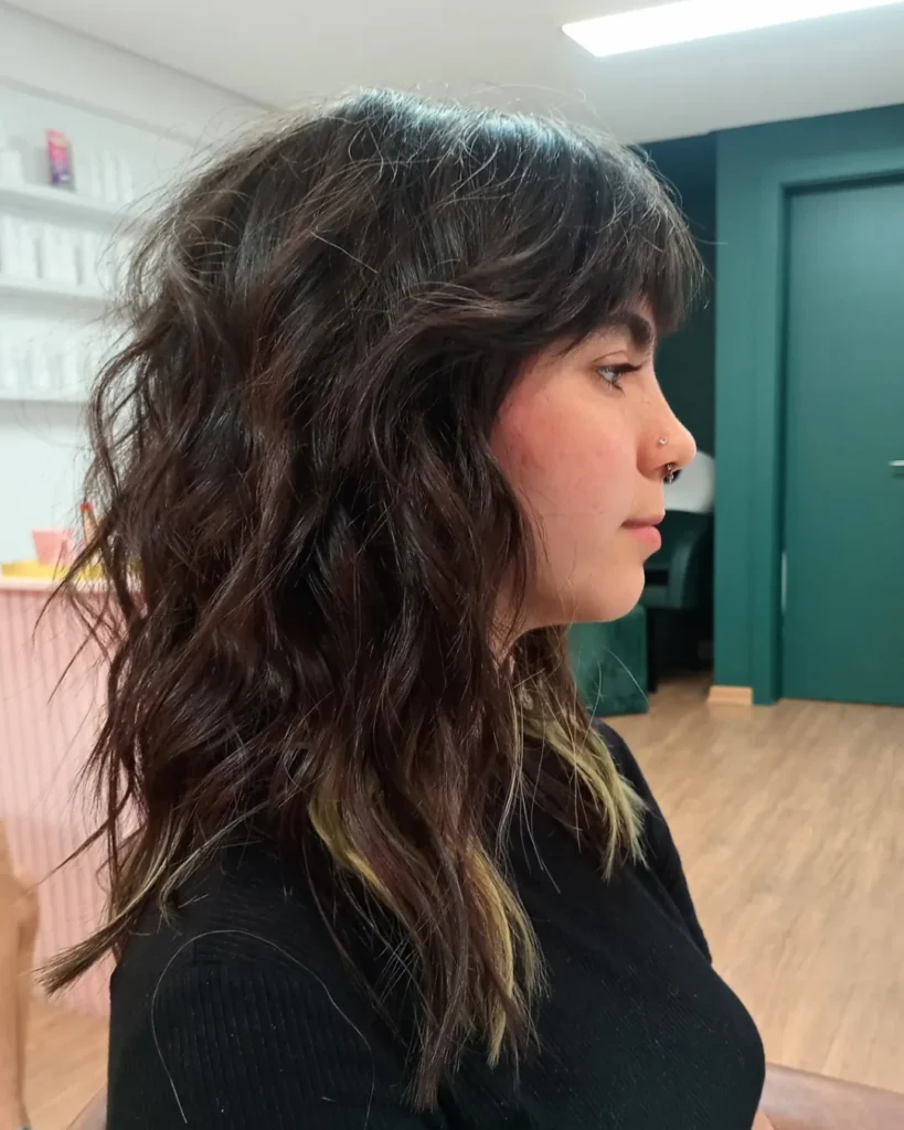 A woman with a medium length wavy shag haircut with choppy layers and natural texture.