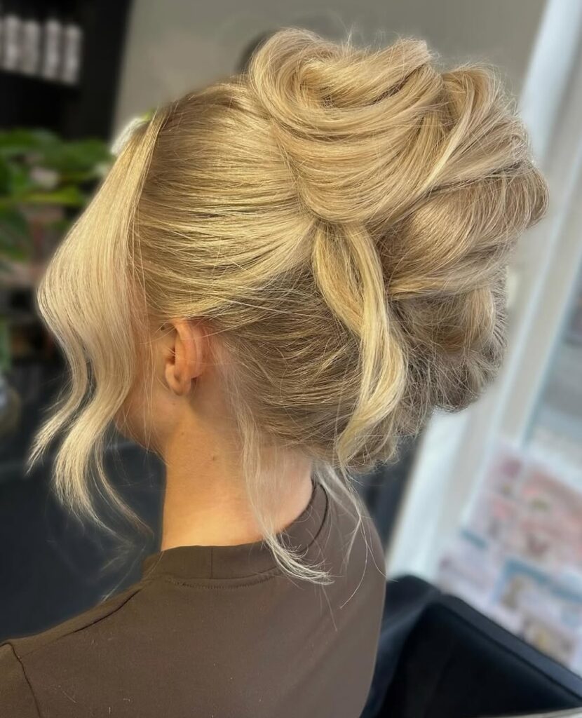 Blonde twisted updo with soft volume and loose face framing strands.