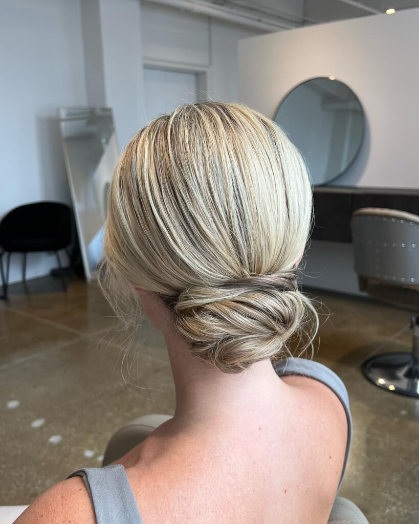 Loose blonde low knot with soft twists and textured finish.