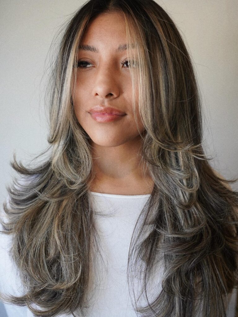 Long layered hair with feathered ends and soft face framing balayage highlights.