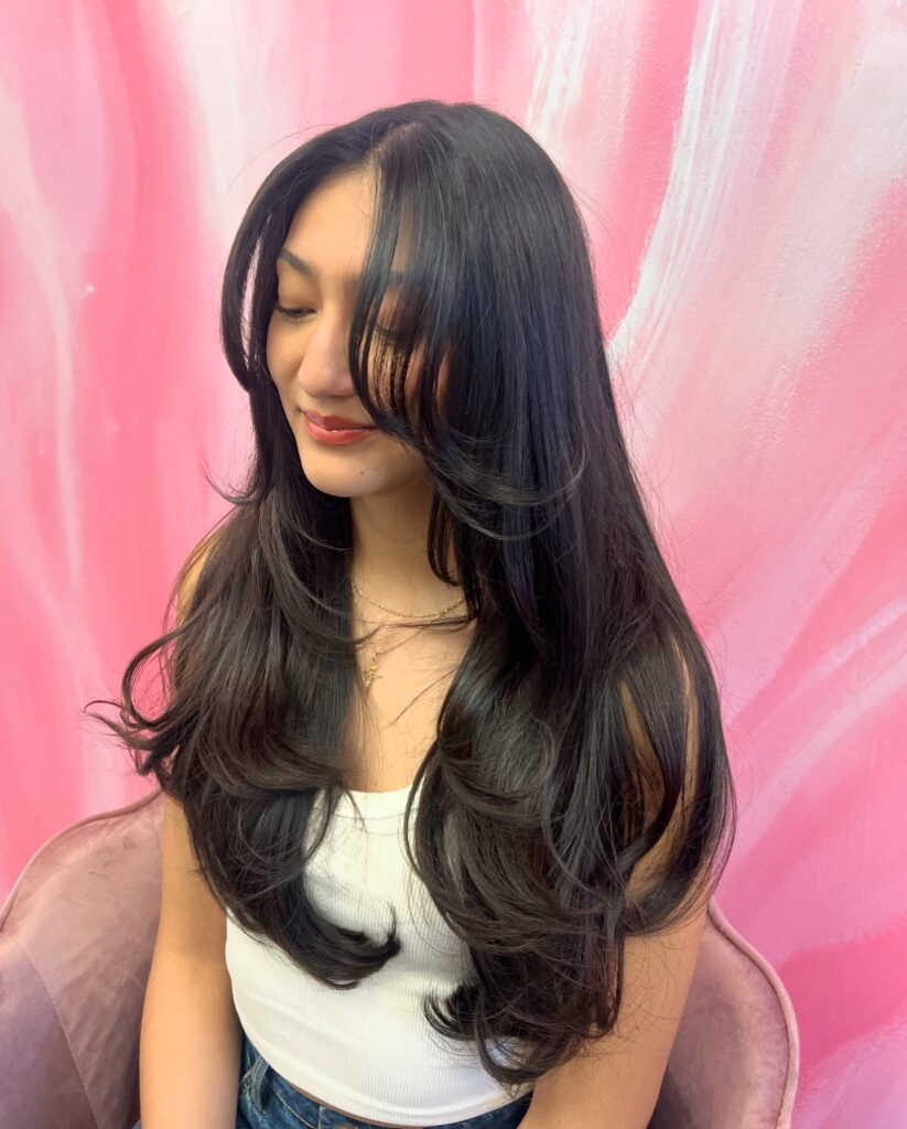 Long straight dark hair with soft layers and curtain face framing pieces.