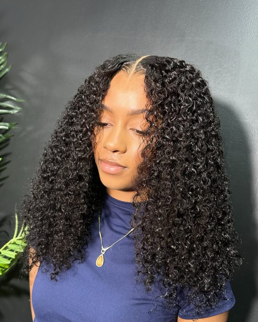 A woman with medium length glossy black hair featuring a sharp middle part and highly defined tight curls.