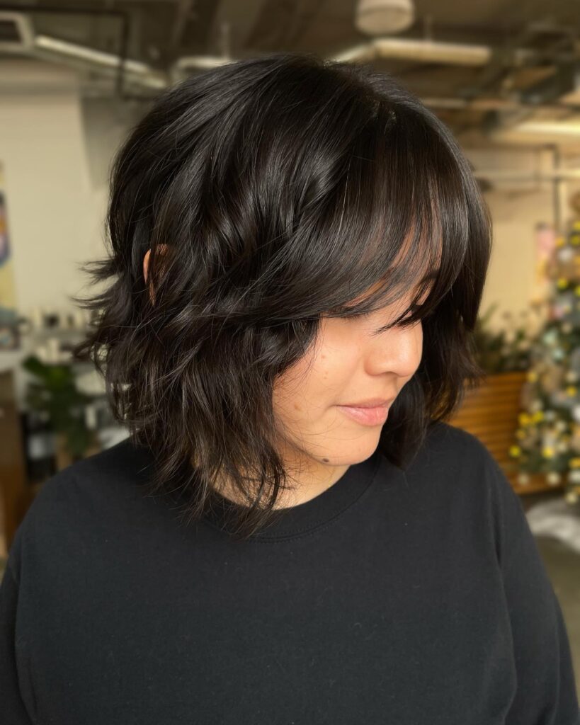 A woman with a short dark brunette shag haircut featuring choppy layers and soft face framing curtain bangs.