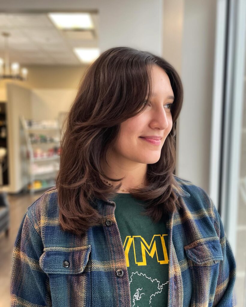 A woman with medium length dark brown hair in a chic layered haircut with symmetrical face framing curtain bangs.