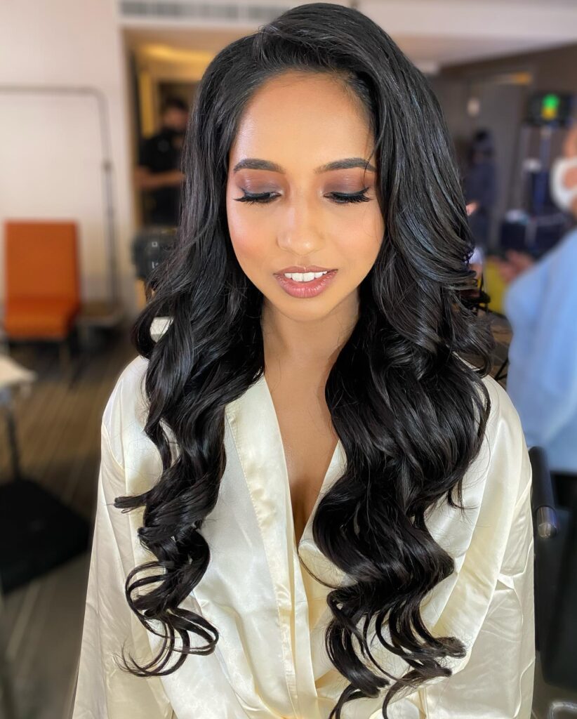 A woman with long jet black hair styled in a deep side part with large bouncy curls.