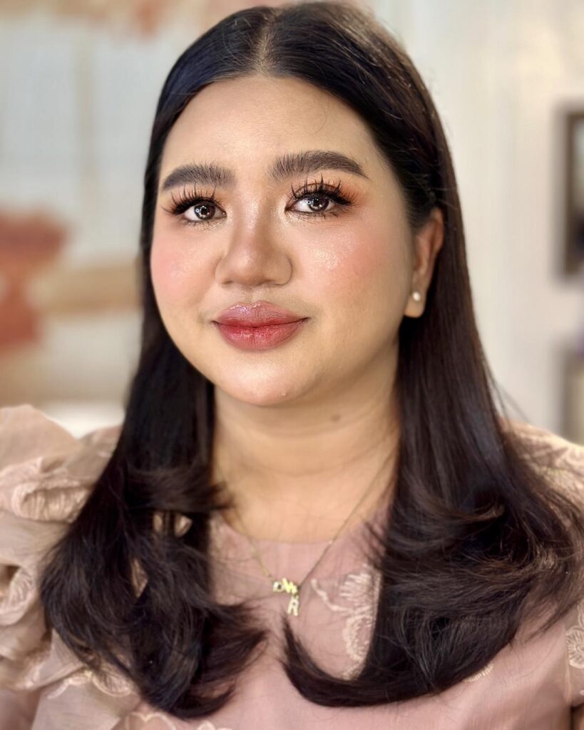 A woman with long dark hair styled in a sleek middle part with the ends curled inward and tucked behind her ears.