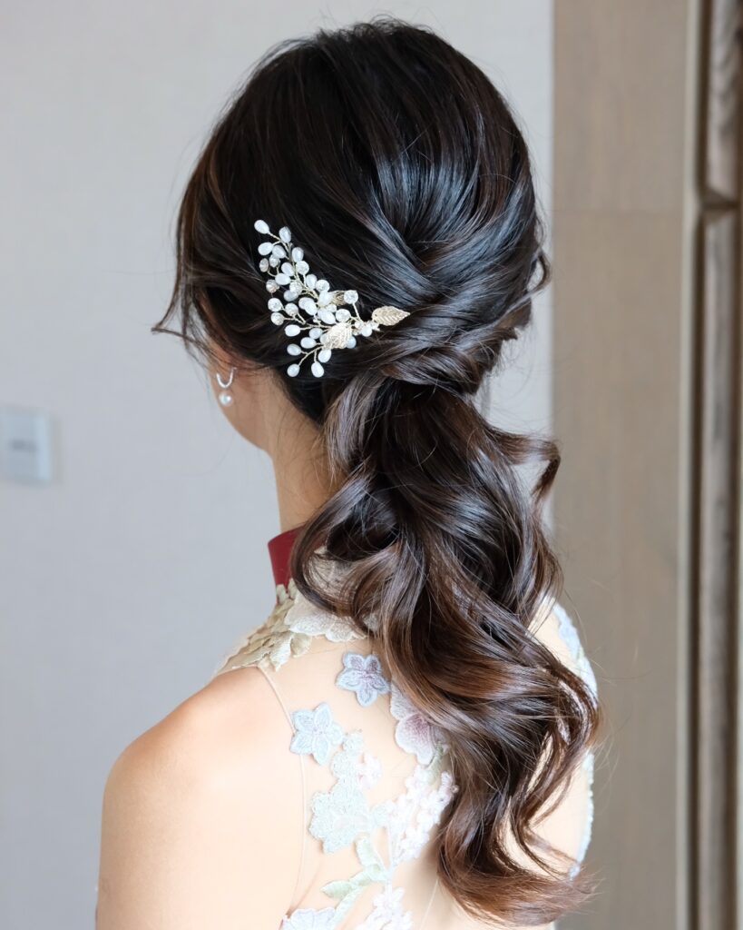 A back view of a woman with dark wavy hair in a twisted low ponytail decorated with a pearl and gold leaf hair clip.