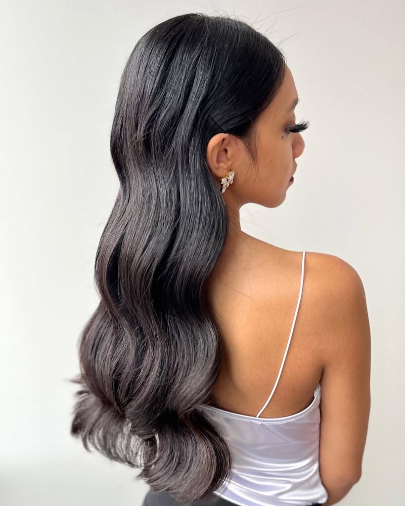 Long dark hair styled in smooth glossy waves for a sleek and refined professional look.