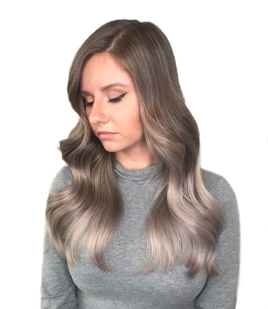 Long ash brown hair with cool toned highlights styled in smooth flowing waves for a refined look.