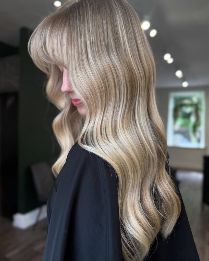 Long icy blonde hair styled in defined glossy waves with a sleek and professional finish.