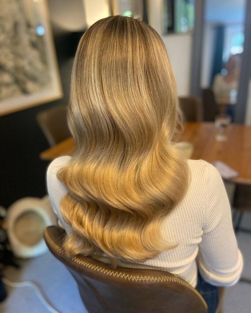 Long blonde hair styled in glossy defined waves with a smooth structured shape.