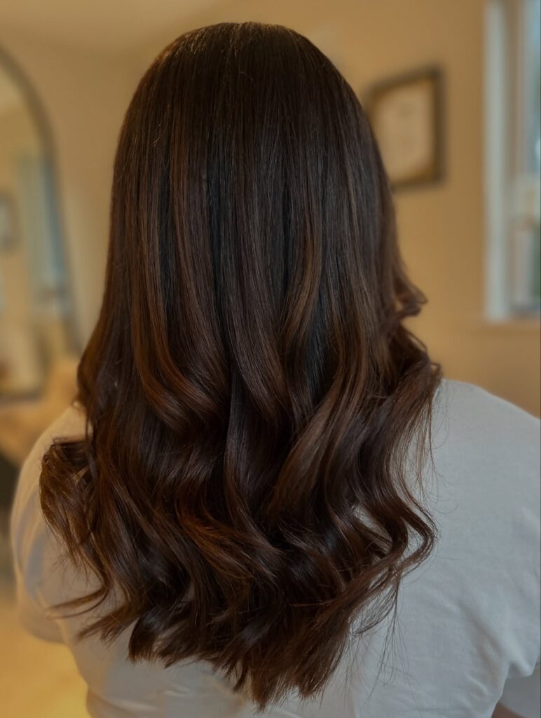 Medium to long brunette hair styled in loose glossy waves with softly curved ends.