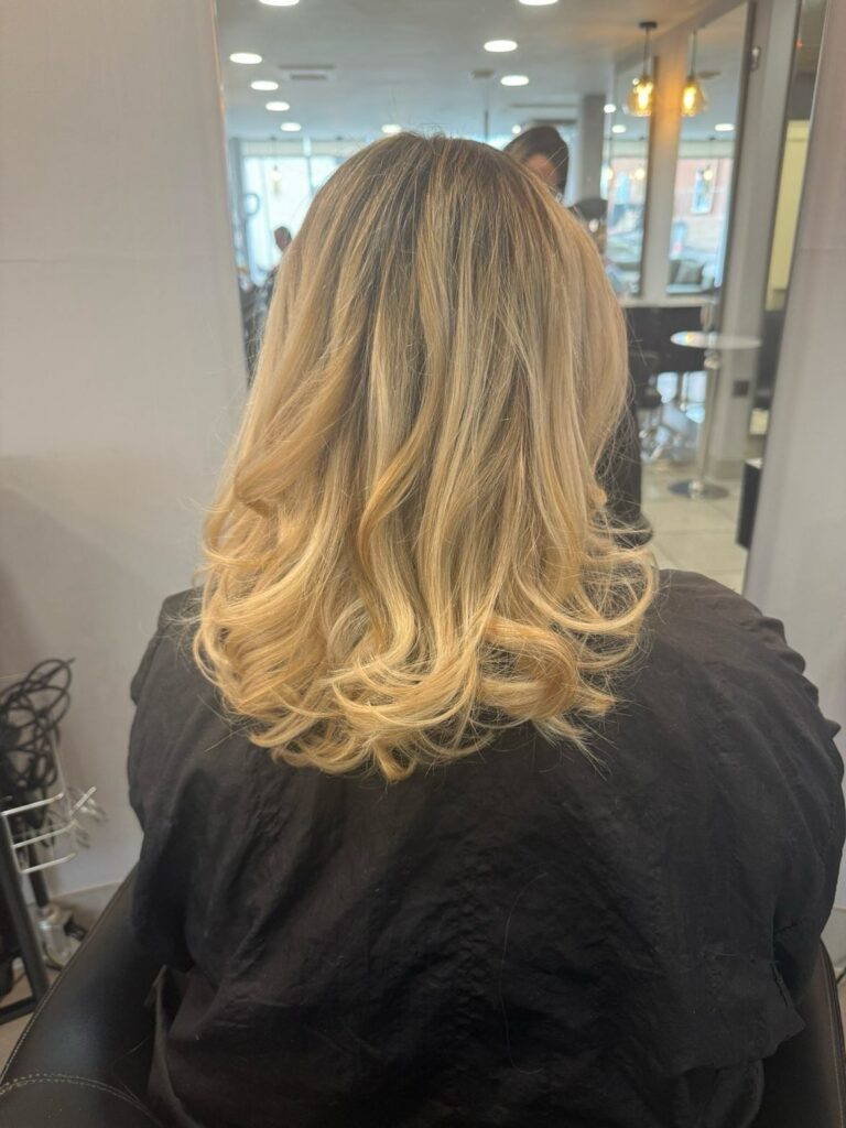 Medium length blonde hair styled in a soft blowout with curved ends and light layers.