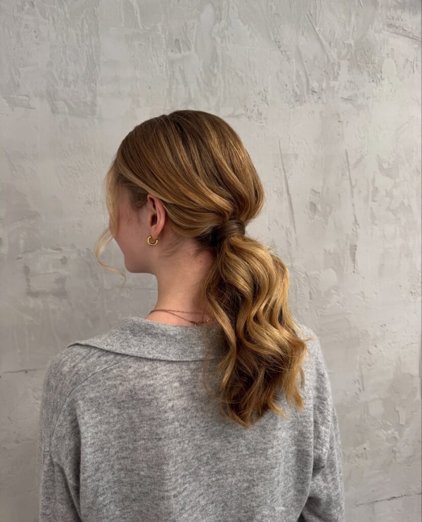 Low ponytail with soft waves and a relaxed polished finish in brunette tones.