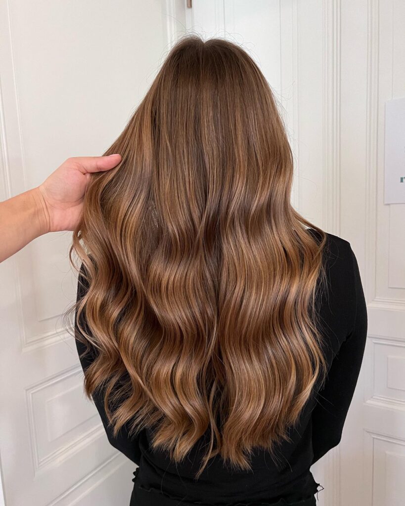 Long brunette hair styled in soft waves with subtle balayage and smooth flowing texture.