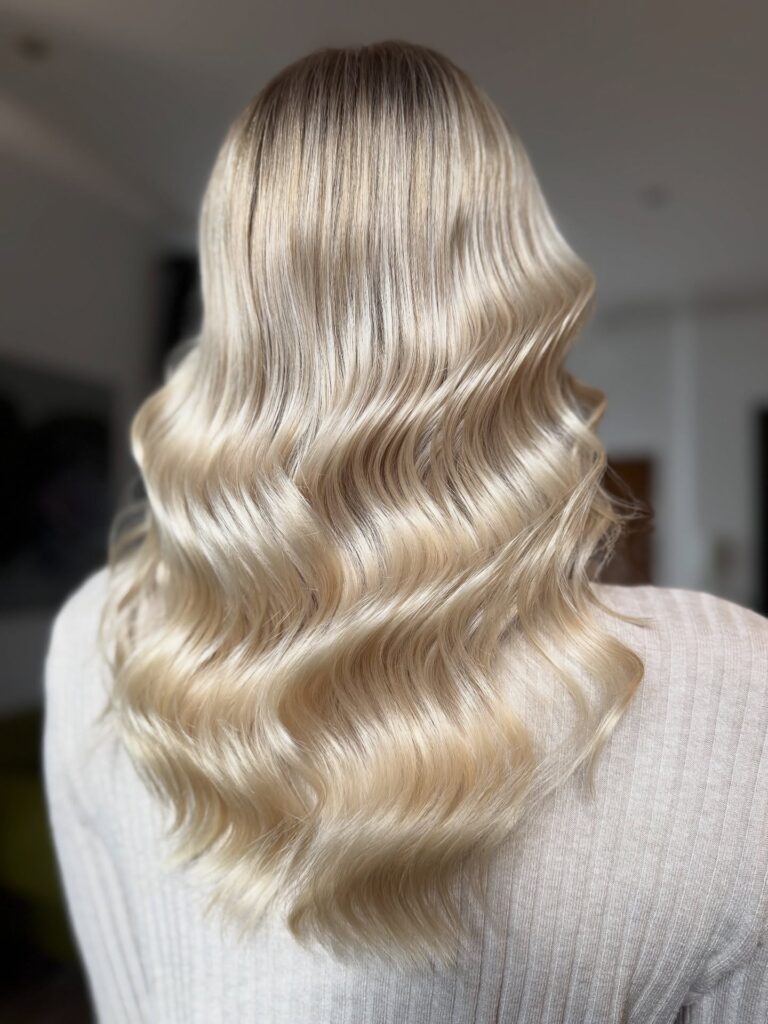 Long blonde hair styled in soft smooth waves with subtle dimension and shine.