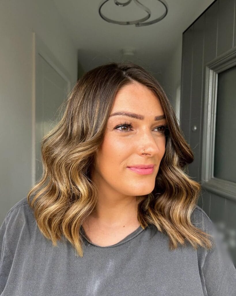 A woman with a wavy bob featuring blonde balayage and soft polished waves.