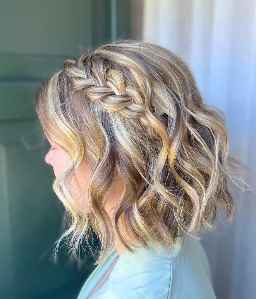 A woman with a short wavy blonde bob featuring a side braid and soft loose waves.