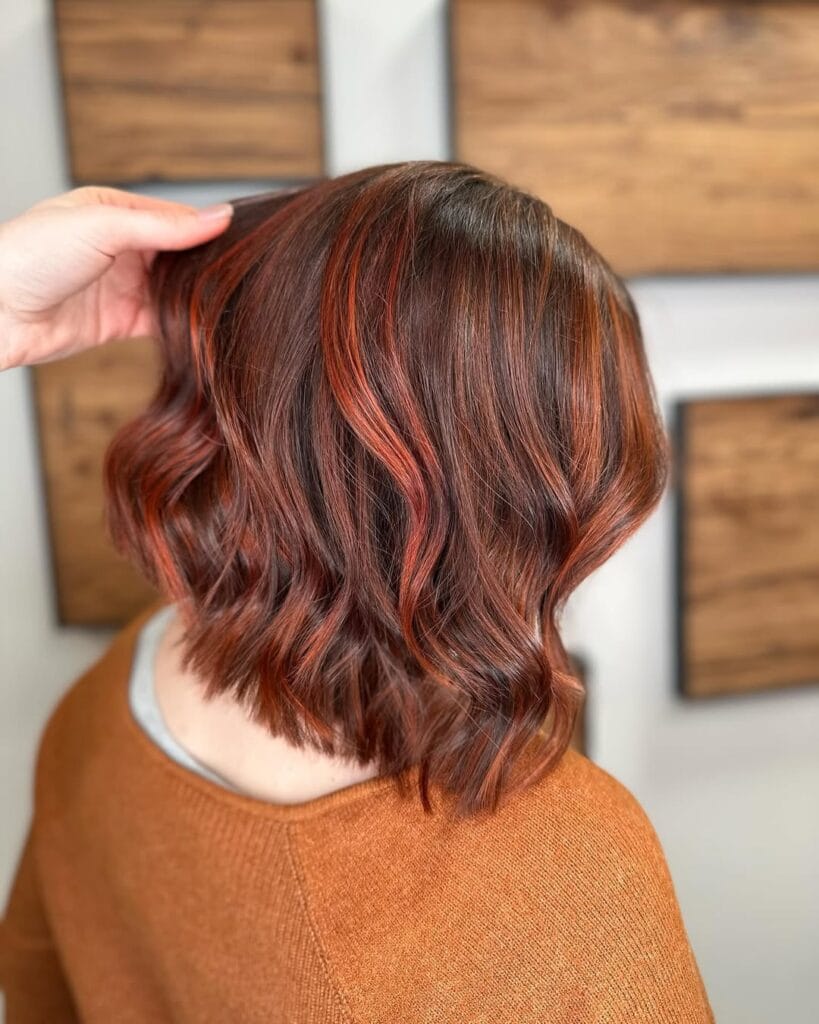 A woman with a short wavy bob featuring copper highlights and soft layered waves.