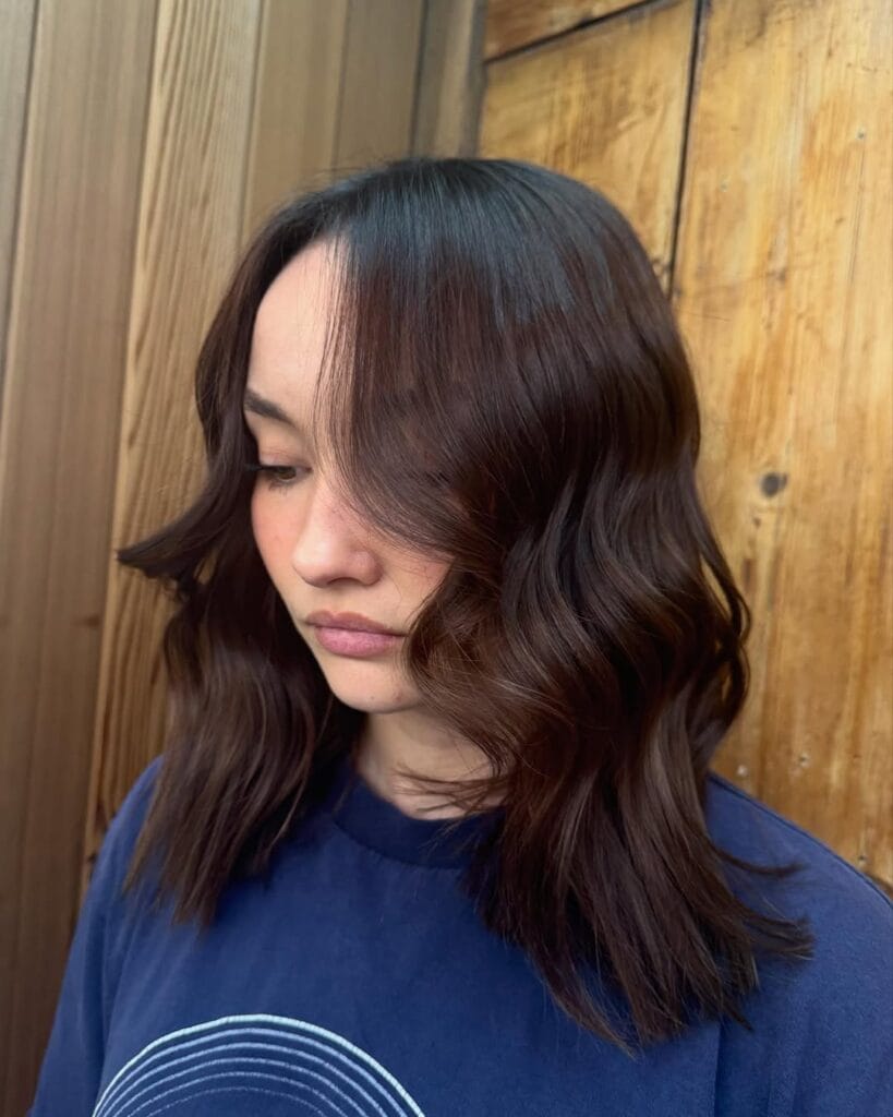 A woman with medium length dark brown wavy hair styled in soft defined waves around the face.