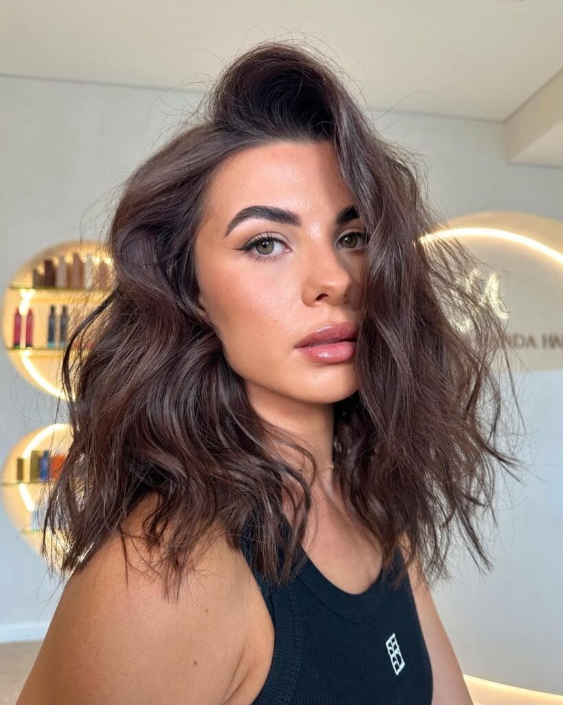 A woman with shoulder length dark brown wavy hair styled with volume and a soft side part.