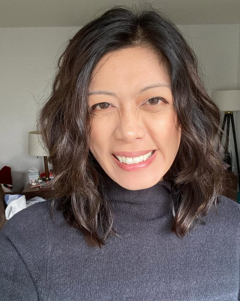 A woman with a dark brown wavy lob styled with soft layers and a side part.