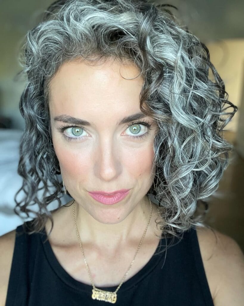 A woman with a short curly bob featuring natural gray and dark tones and defined soft curls.