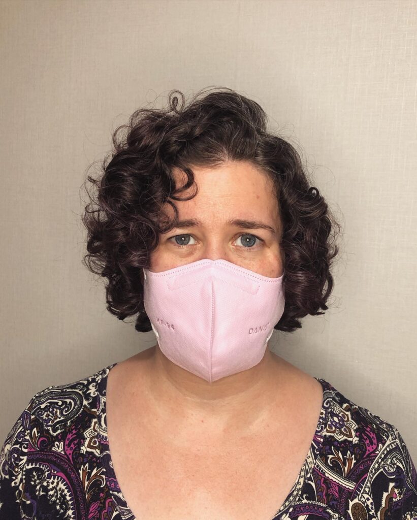 A woman with a chin-length curly bob in a deep brunette shade and a soft side part.