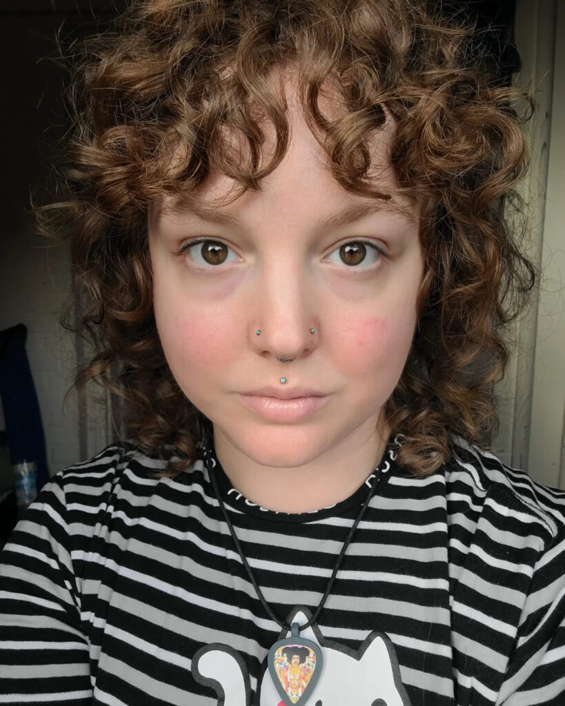 A woman with a medium brown curly shag haircut and full curly bangs looking directly at the camera.