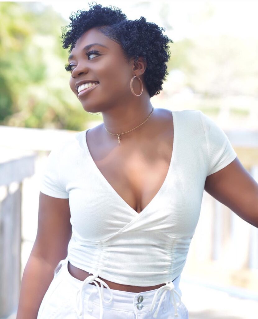 A smiling woman with a short tapered natural hairstyle featuring tight black coils and a side part.