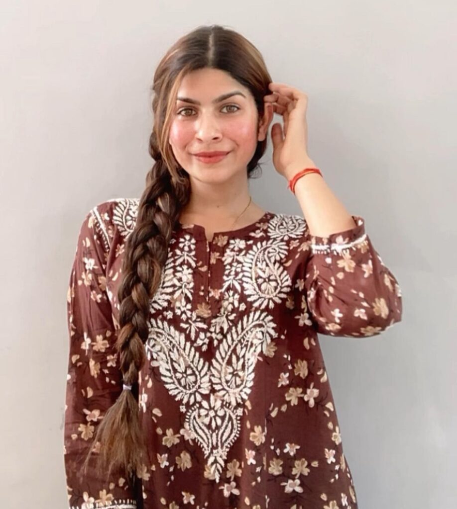 A woman with long, thick, brown hair styled in a chunky side braid resting over her shoulder.