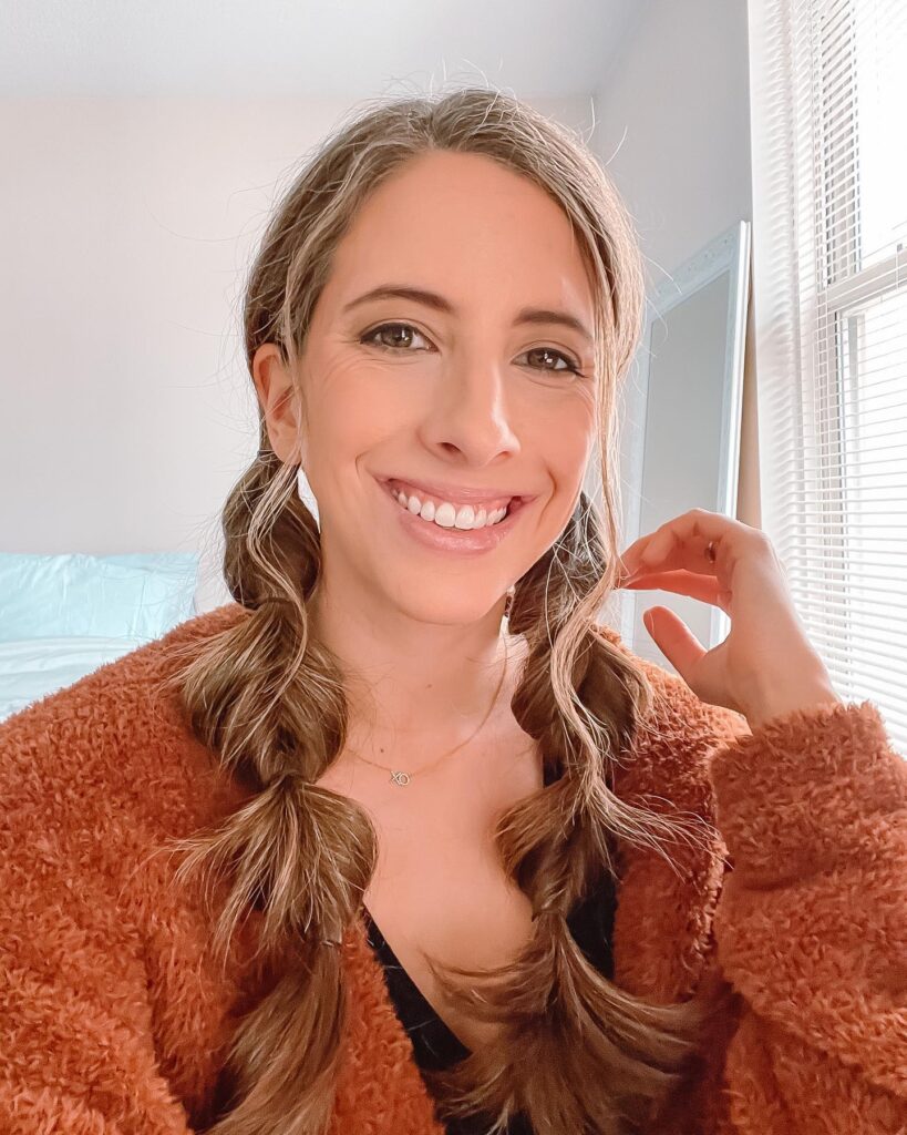 A smiling woman with long brown hair styled into two thick and voluminous bubble braids resting on her shoulders.