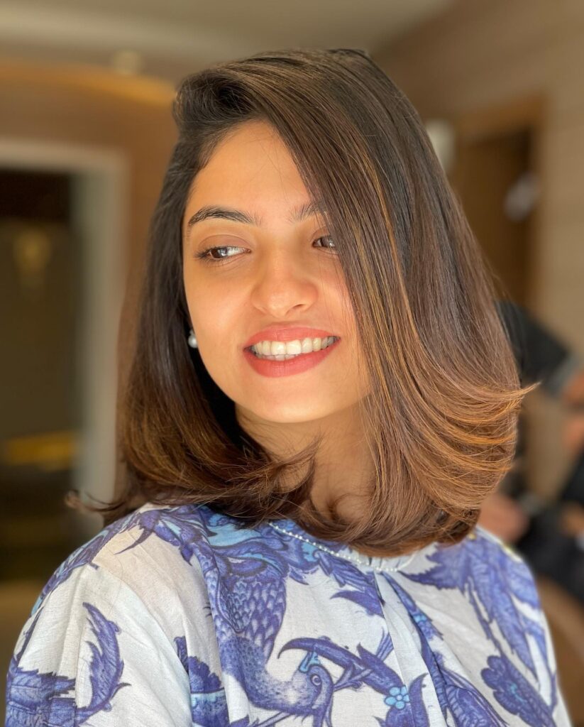 A woman with a polished shoulder-length chestnut brown blowout featuring voluminous layered ends that flip outward.