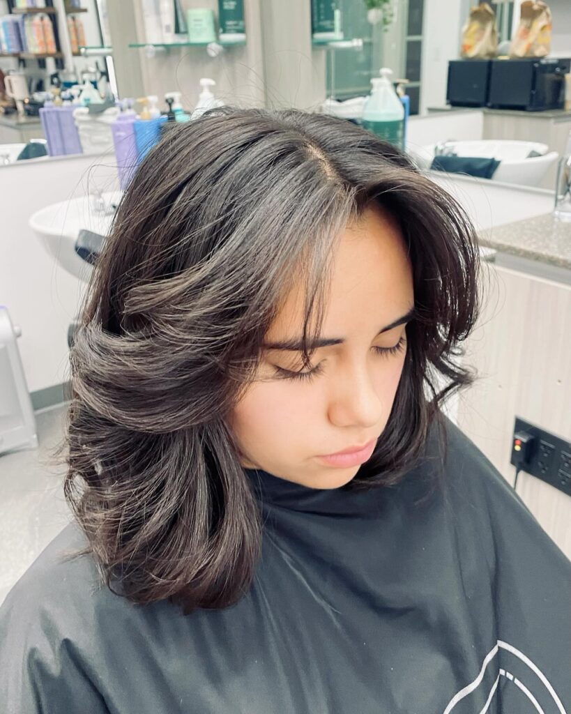 A woman with voluminous shoulder-length dark espresso hair featuring thick face-framing layers and feathered ends.