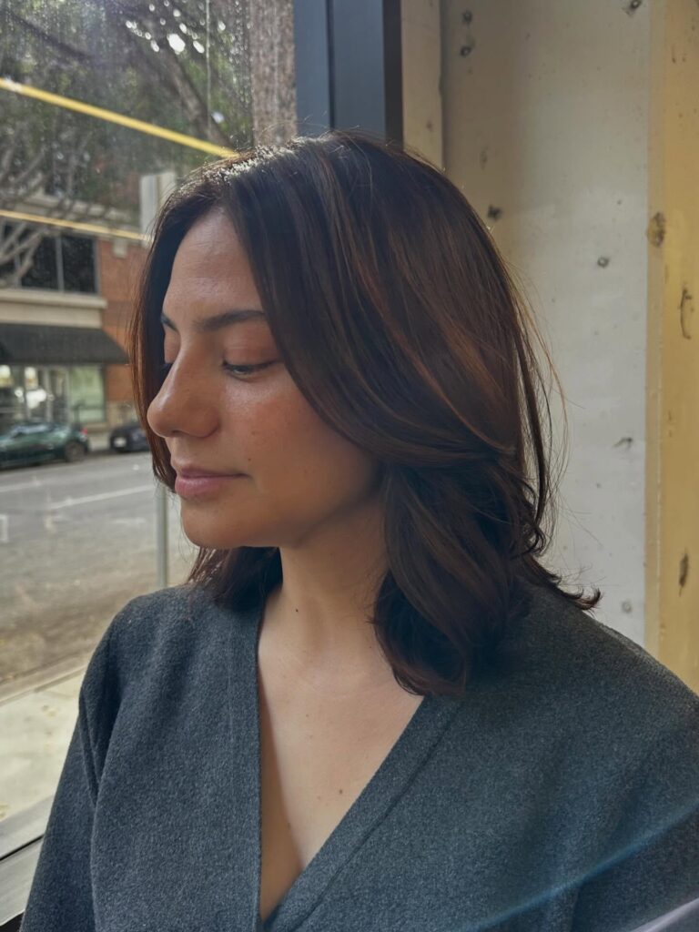 A side profile of a woman with a glossy mahogany brown shoulder-length lob featuring soft chin-length layers.