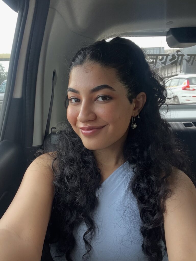 A woman with long dark cascading curls wearing a half-up hairstyle.