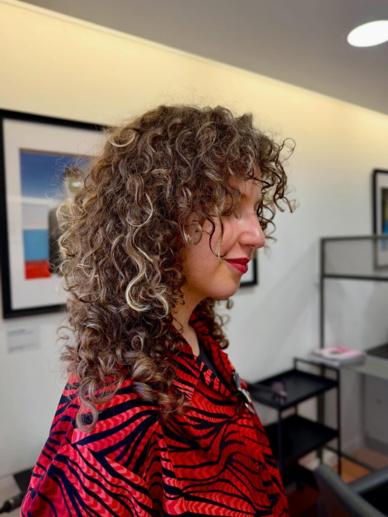 A woman with medium-length ashy brown curly shag and blonde highlights.