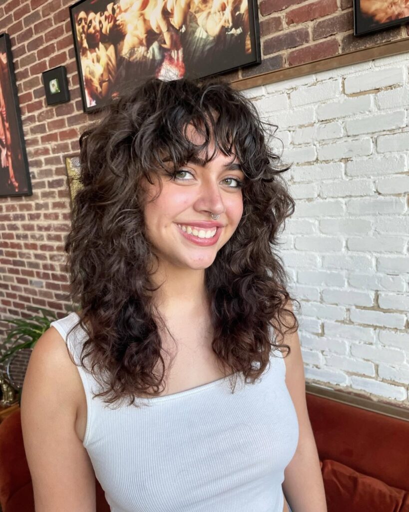 A woman with a medium-length dark espresso curly shag and face-framing bangs.