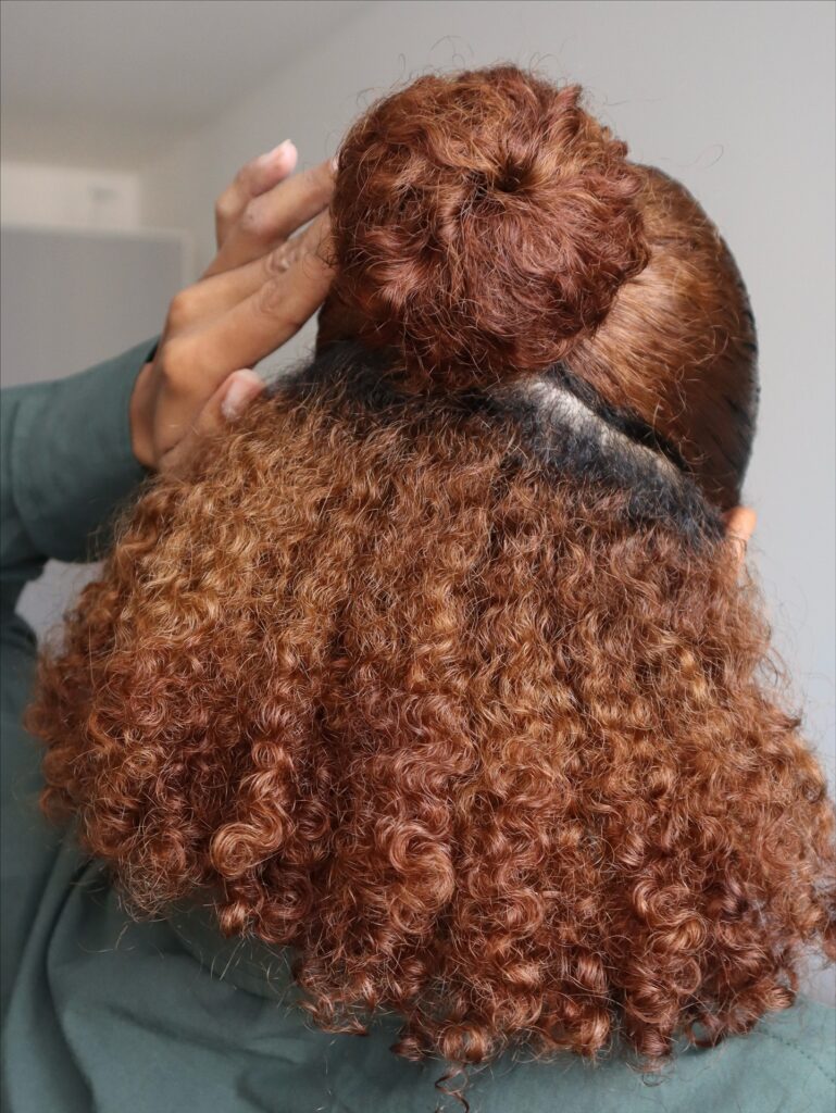 A woman with medium-length cinnamon brown curls styled in a half-up topknot bun.