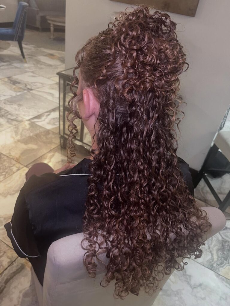 A woman with long, curly mahogany hair styled in a voluminous half-updo.