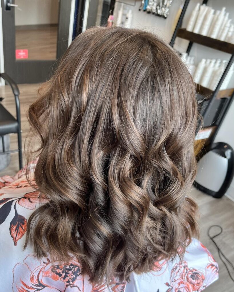 A rear view of a woman with medium-length dark brown hair styled into bouncy, defined curls with subtle warm highlights.