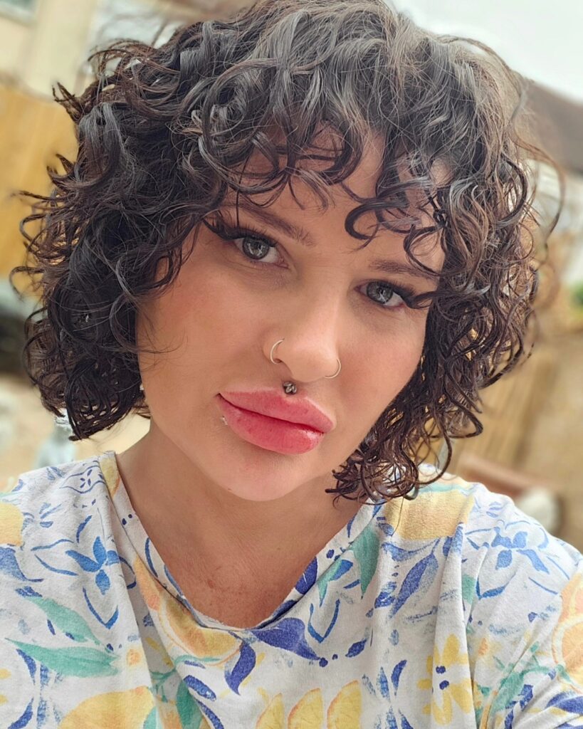 A woman with a glossy black chin-length bob and curly bangs is looking at the camera.