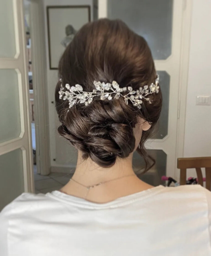 A woman from behind wearing a smooth, chocolate-brown twisted low bun decorated with a shimmering silver crystal hairvine.