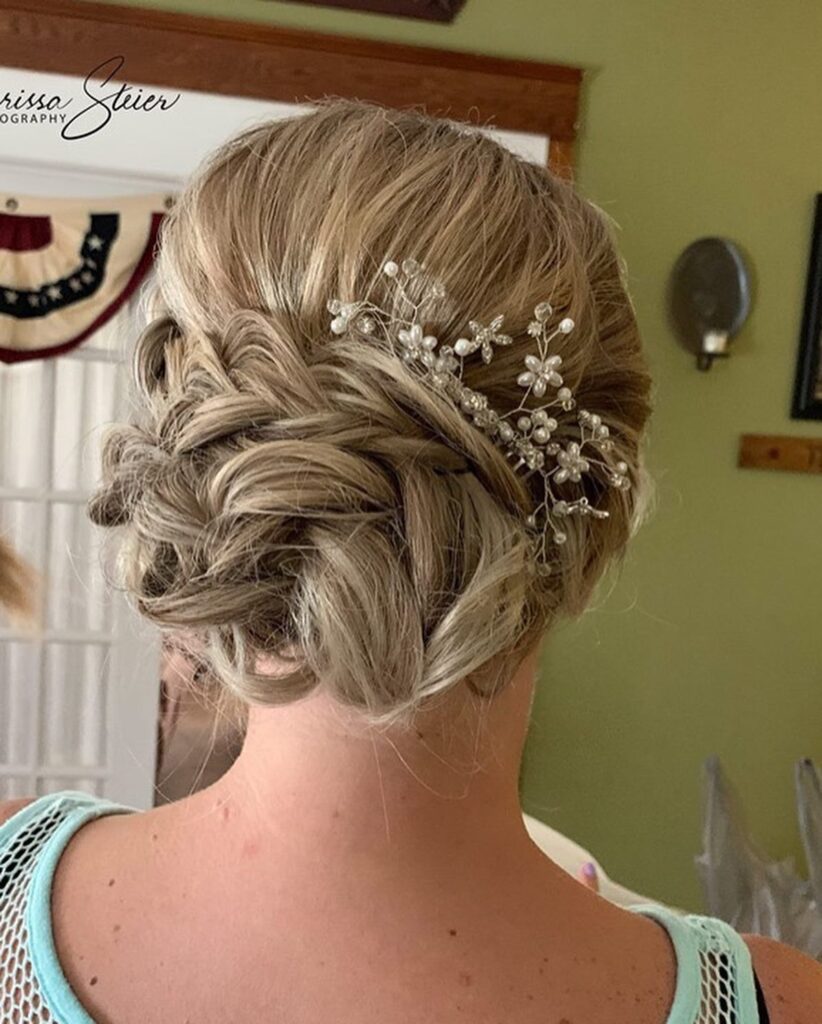 A woman from behind showing a messy braided low bun in ash-blonde hair decorated with a delicate pearl and crystal hair vine.