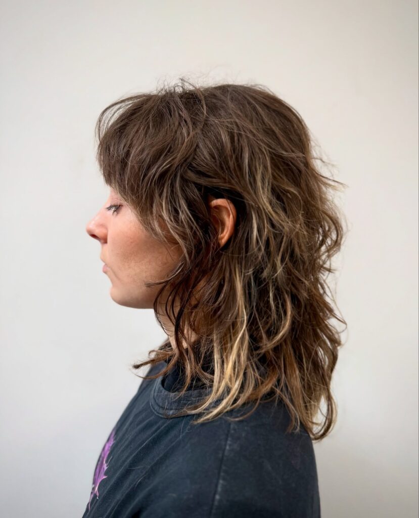A side profile of a woman with a choppy layered shoulder-length shag haircut featuring messy texture and bangs.
