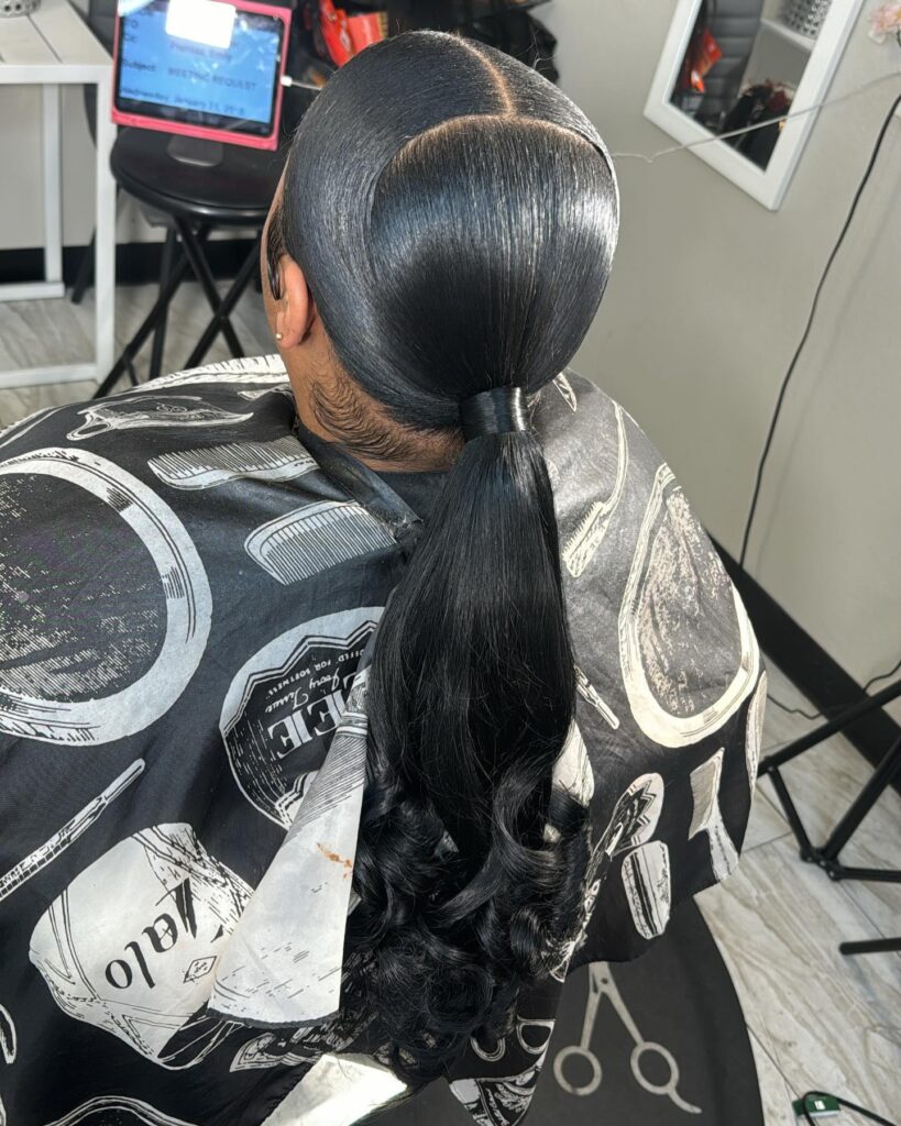 A woman with sleek black hair in a low ponytail featuring a sharp middle part and voluminous bouncy curls at the ends.