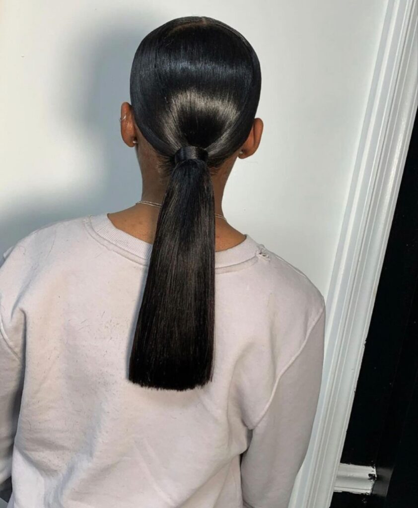 Rear view of a woman with a sleek low ponytail featuring a blunt, straight edge at the bottom and a glossy black finish.