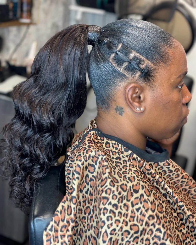 A woman with a high, wavy dark brown ponytail featuring intricate small tied hair sections along the side of her head.