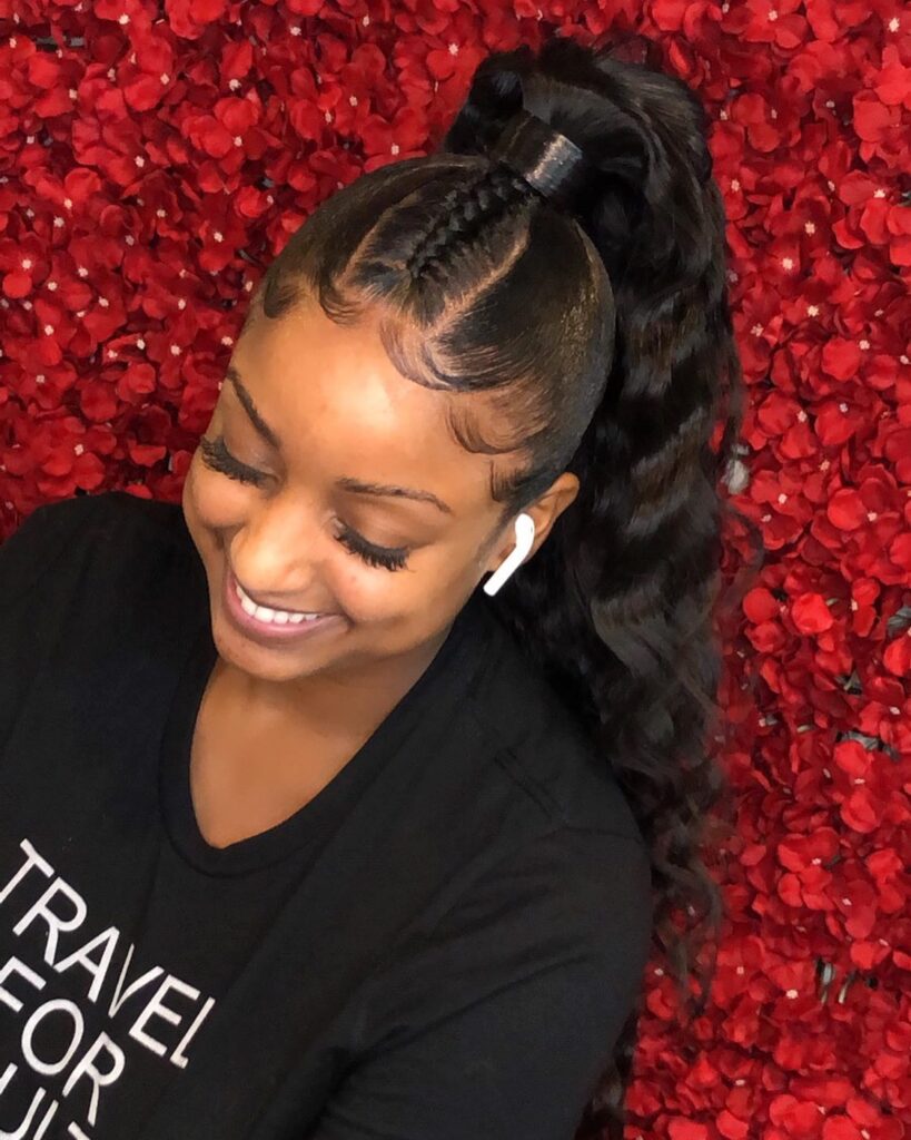 A woman smiling with a high, wavy black ponytail that features a central braid on top and perfectly styled, swooped baby hairs.